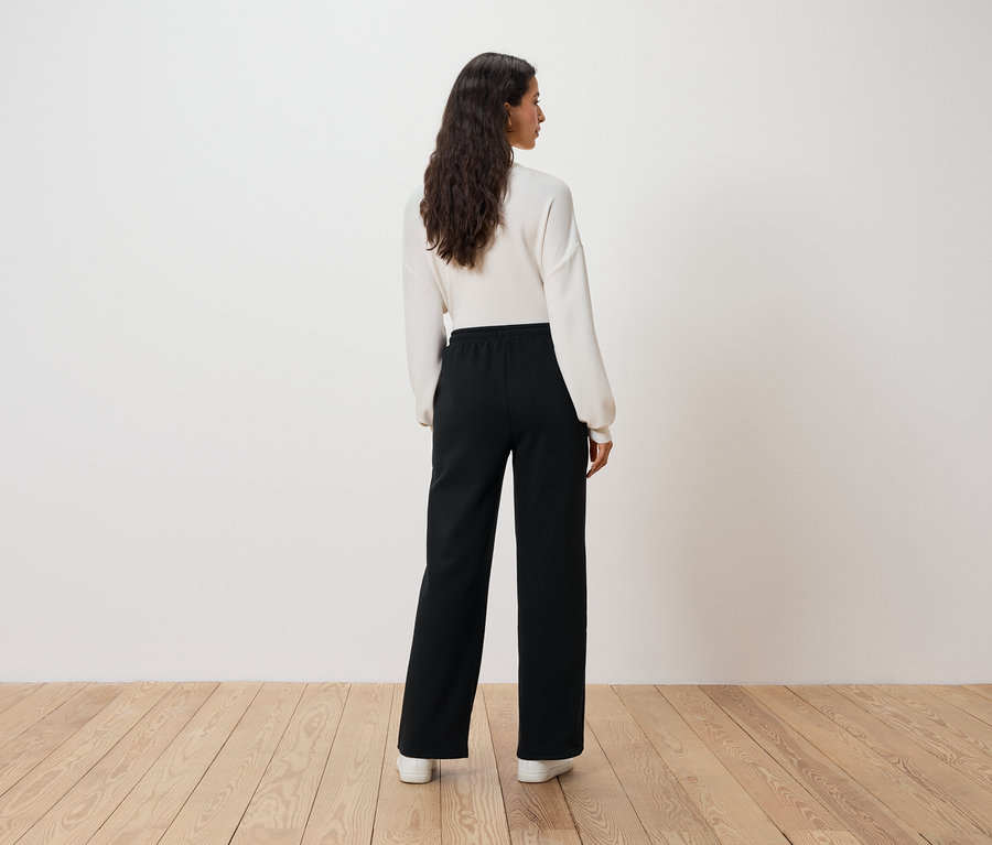 Une femme portant un pull blanc et un pantalon noir, vue de dos.