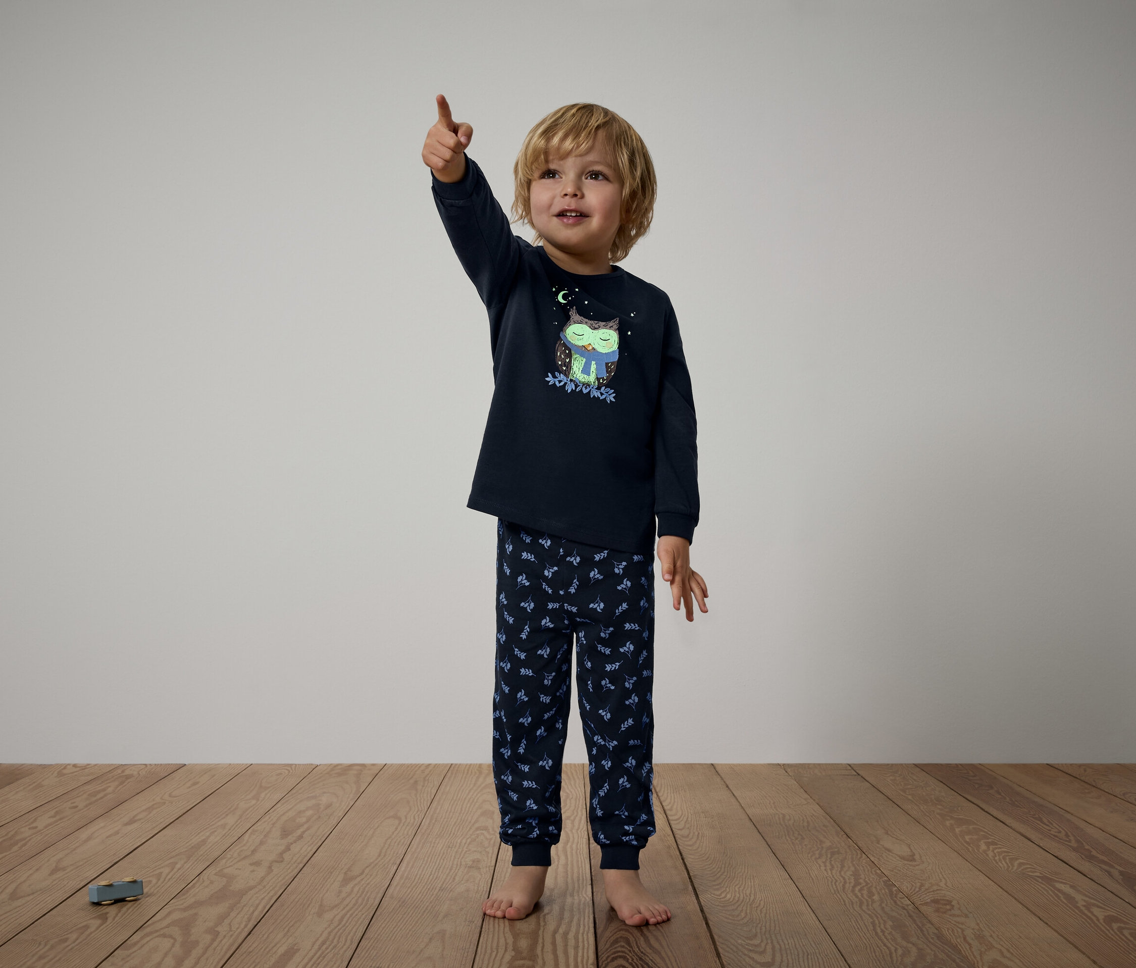 Garçon en pyjama bleu marine avec motif de hibou pointant du doigt vers le haut.