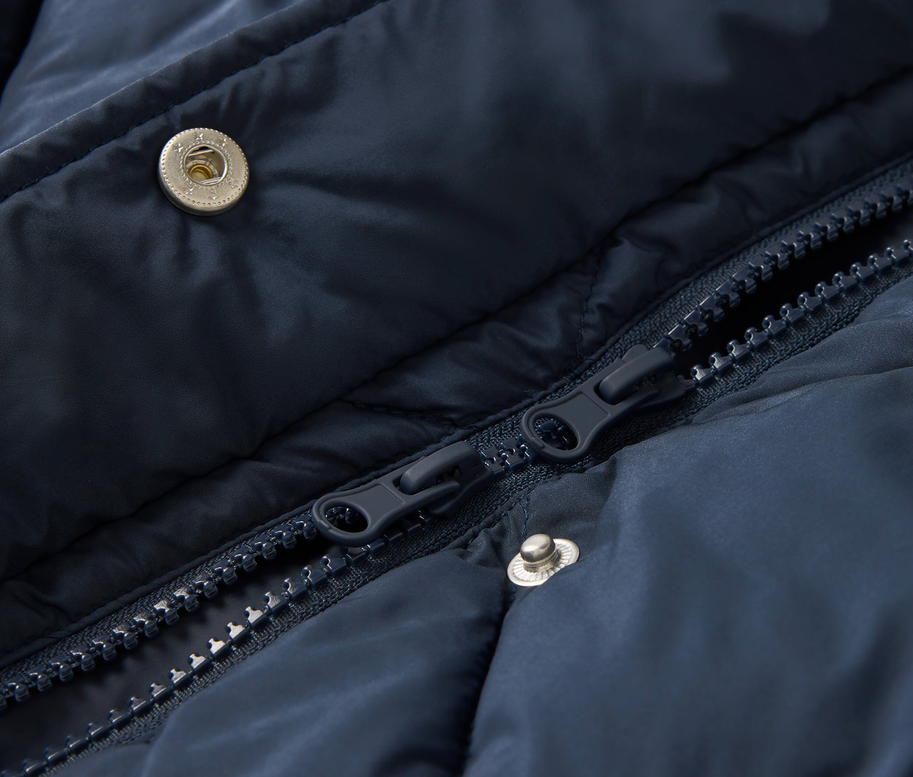 Détail d'une veste matelassée bleu marine avec fermeture éclair et boutons-pression.