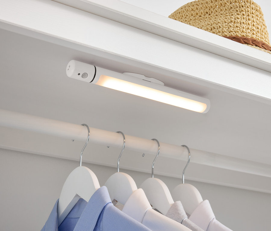 Dans le placard se trouvent une lampe LED blanche, des chemises suspendues à des cintres blancs en dessous et un chapeau de paille sur le dessus.