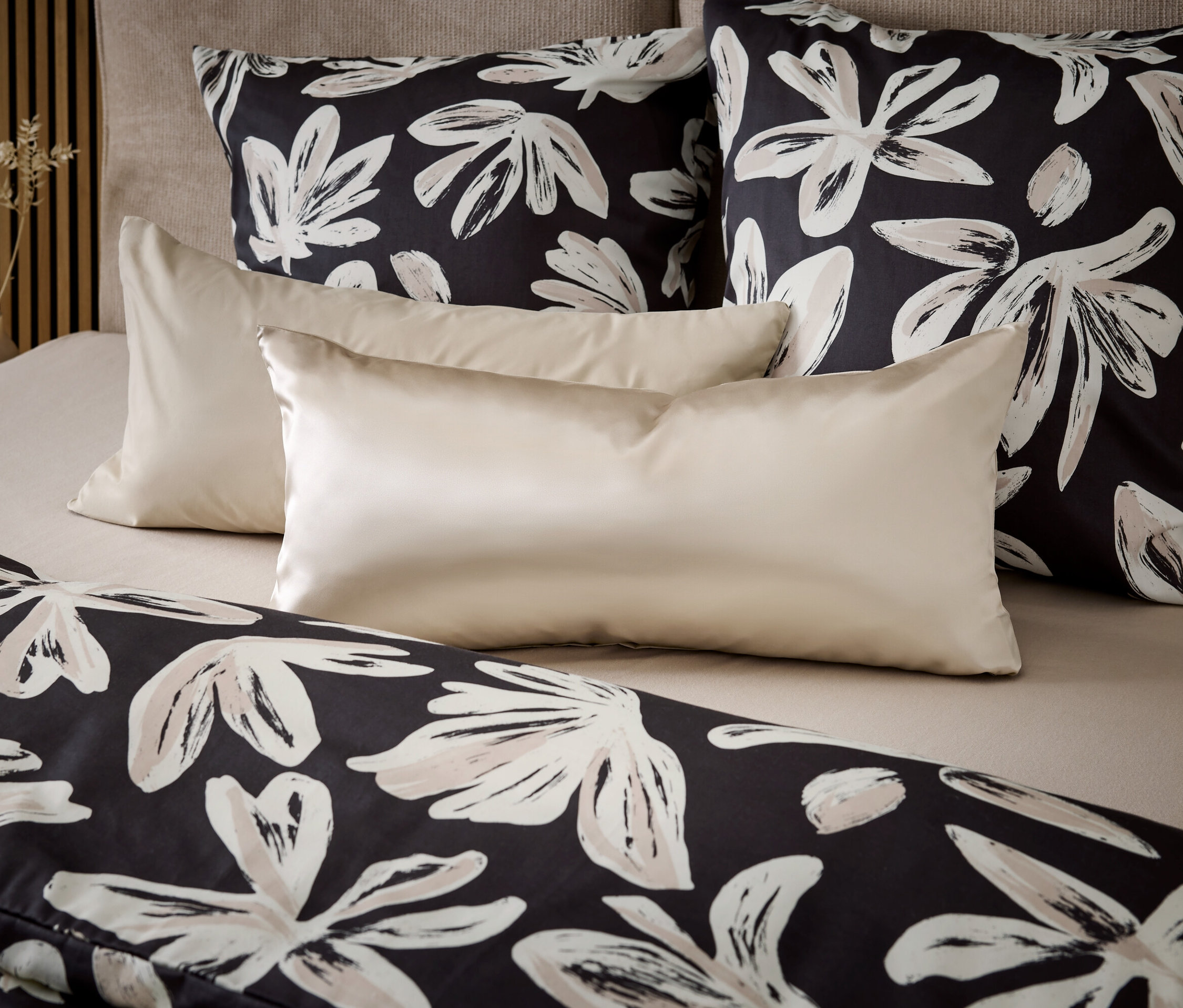 Deux coussins à fleurs noirs et blancs et deux coussins crème sont posés sur le lit.