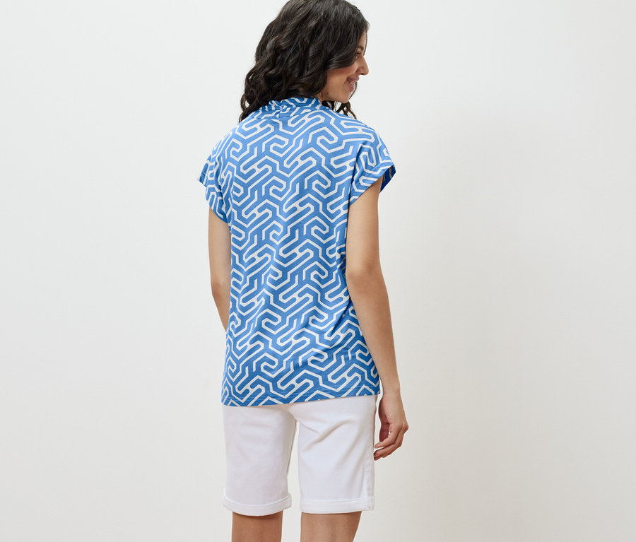 Une femme porte une blouse bleue à encolure en V et un short blanc.