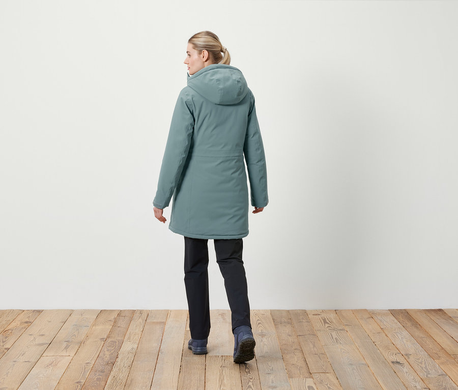 Une femme, dos à la caméra, porte une veste à capuche et un pantalon foncé.