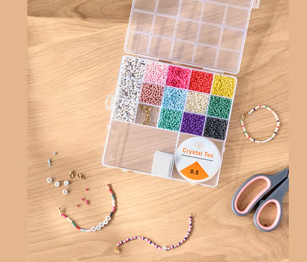 Kit de perles DIY ouvert avec des perles colorées, de la ficelle et des ciseaux sur une table en bois.
