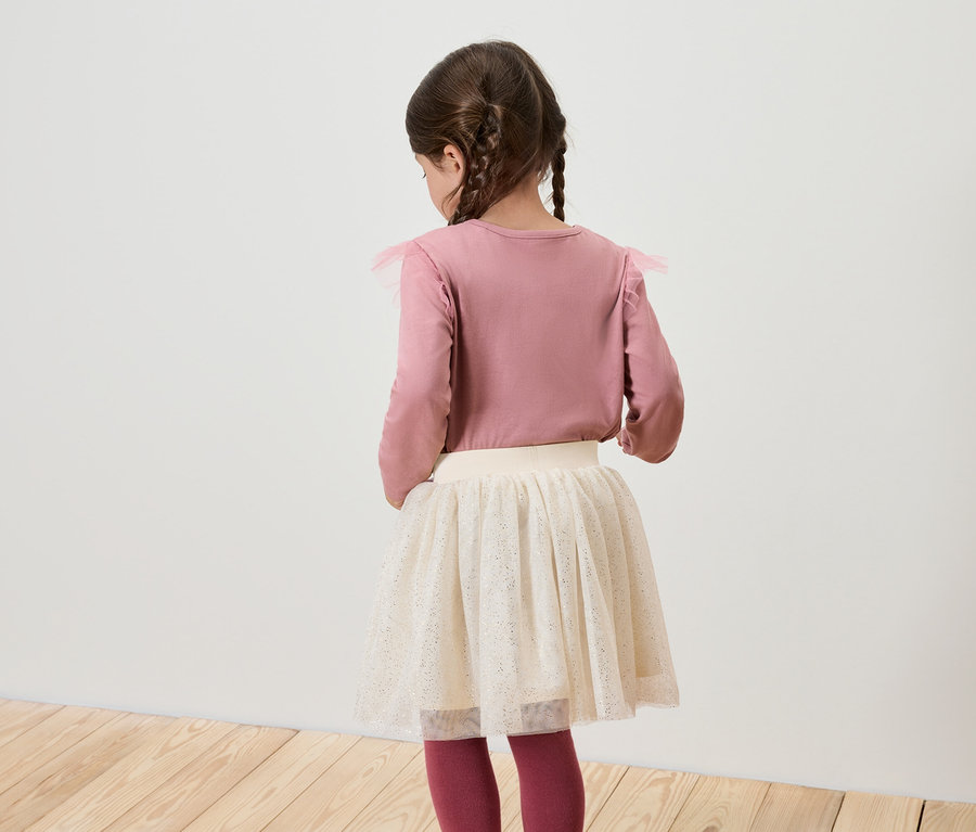 Une fille, vue de dos, porte un t-shirt rose à manches longues et une jupe blanche.