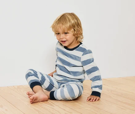 Garçon assis sur un plancher en bois en pyjama rayé.