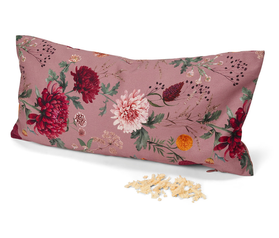 Un coussin oblong à motif floral sur fond rose repose sur une surface blanche à côté d'un tas de rembourrage.
