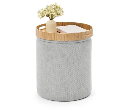 Tabouret gris en tricot avec un plateau en bois sur lequel reposent un vase avec des fleurs et un livre.