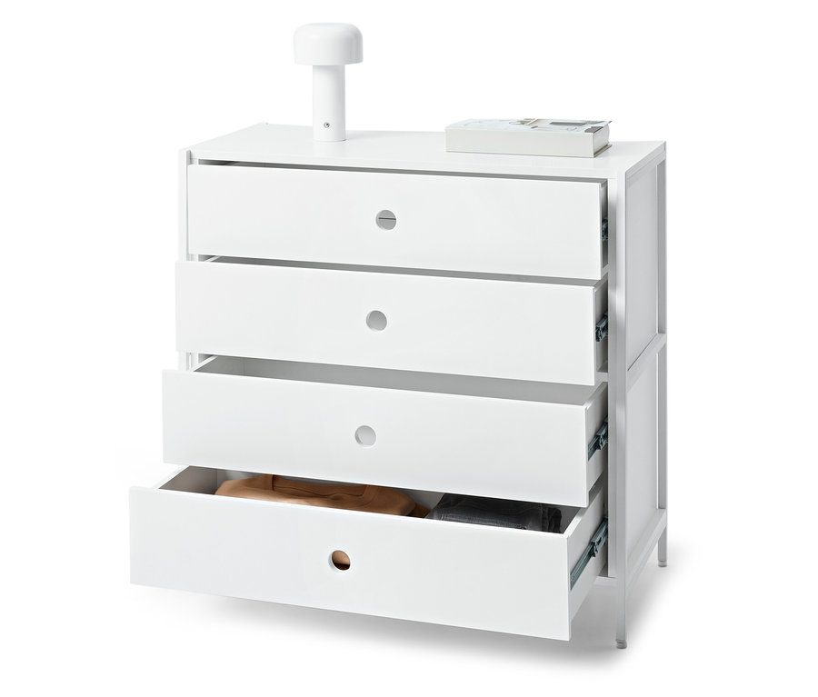 Commode blanche avec quatre tiroirs dont un ouvert, sur laquelle reposent une lampe et un livre.