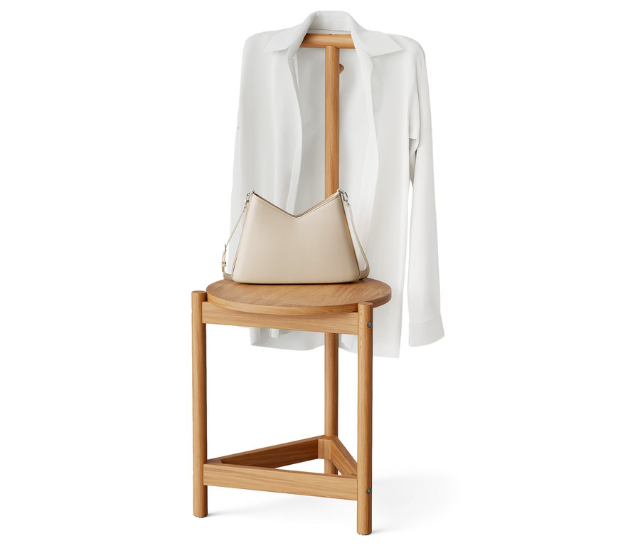 Un sac à main beige et une chemise blanche reposent sur un tabouret en bois.