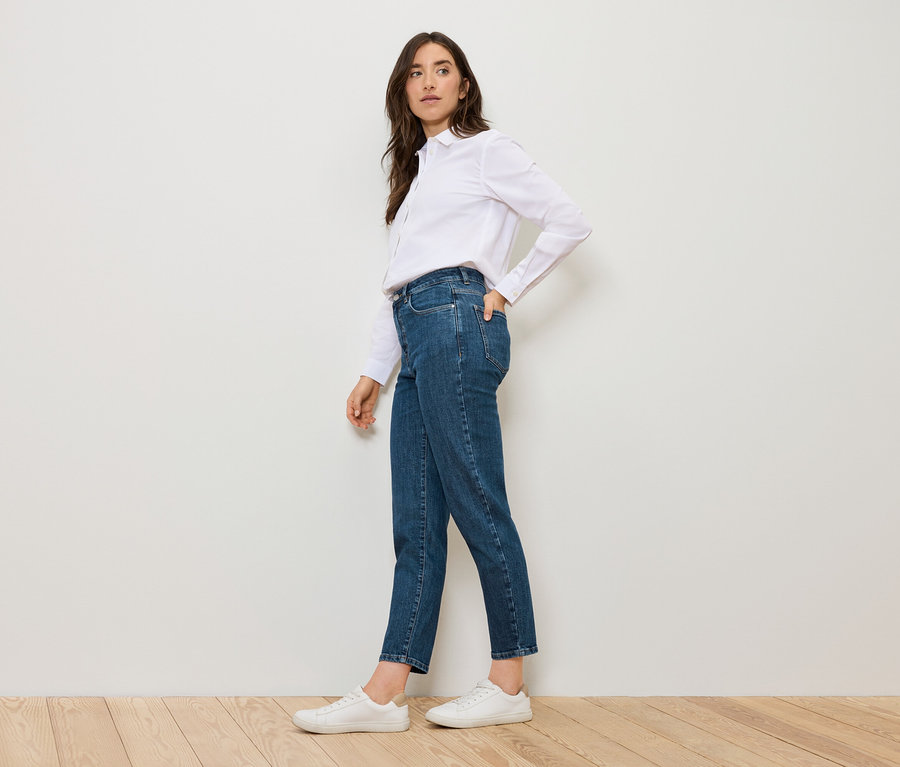 Femme posant en Mom Jeans – Coupe »Nyla« bleues et chemise blanche.