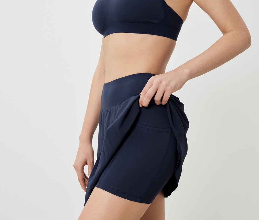 Une femme pose en soutien-gorge de sport et jupe de sport bleu foncé.