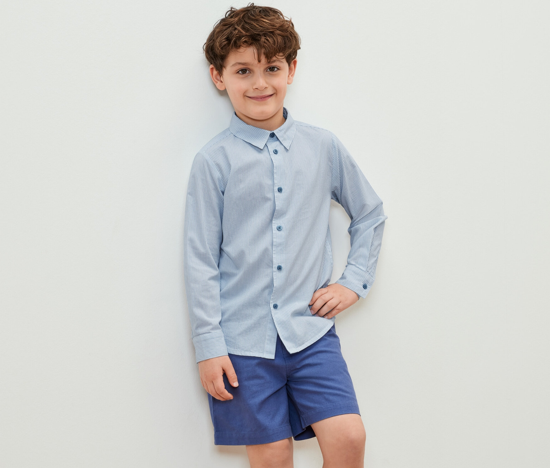 Garçon posant en chemise pour enfant et short bleu.