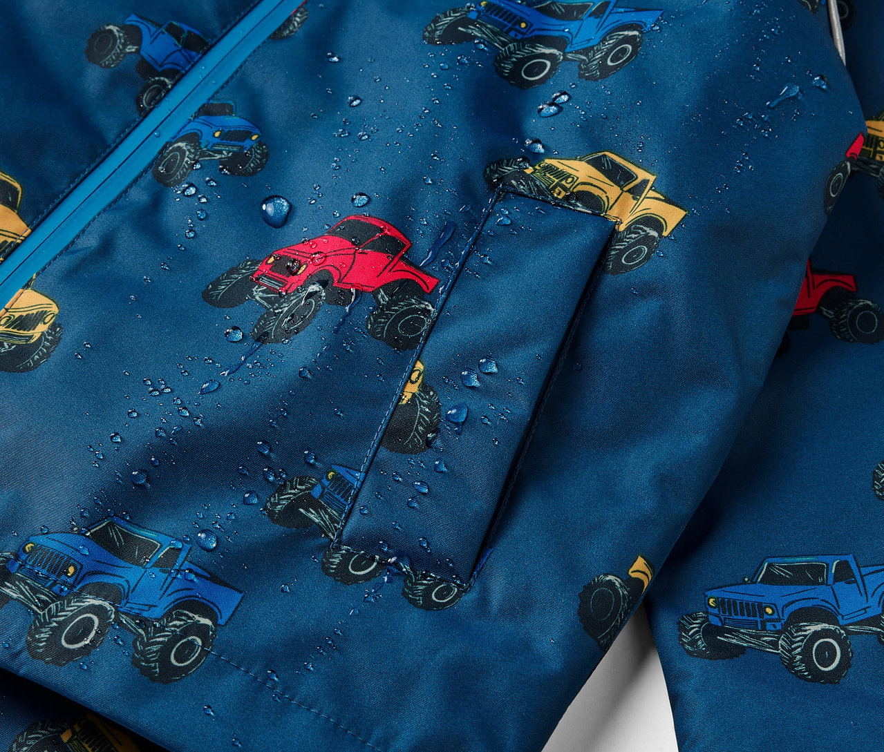 Détail d'une veste imperméable thermique pour enfants avec un motif de monster trucks.