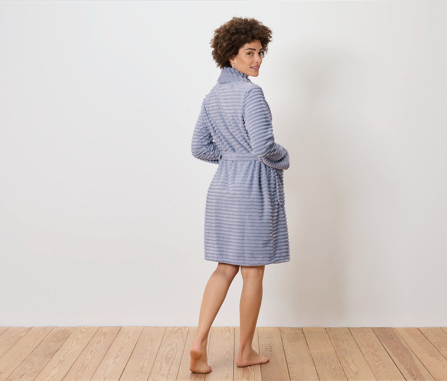 Une femme regarde par-dessus son épaule et pose en peignoir bleu sur un plancher en bois.
