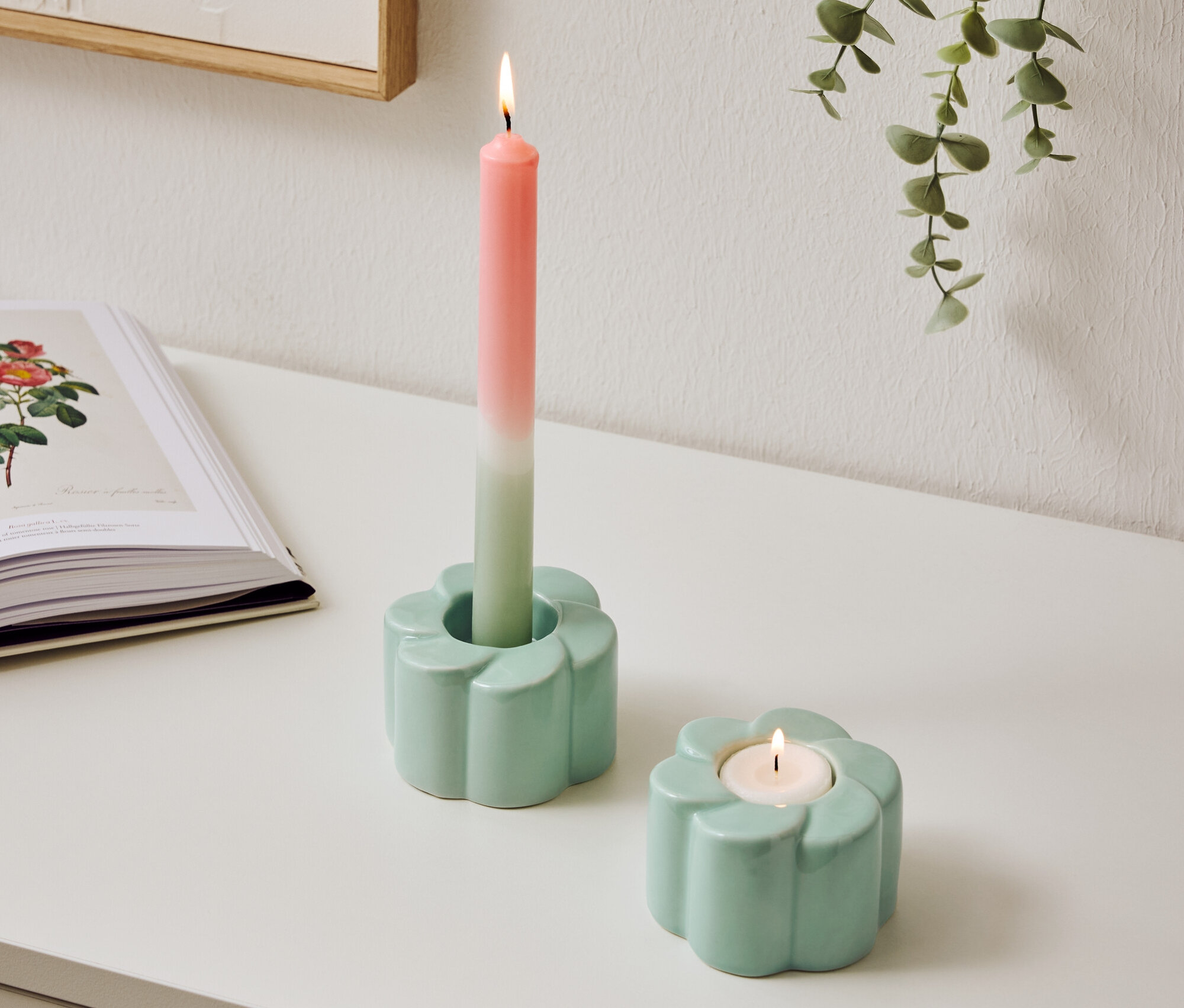 Deux bougeoirs bleu clair en forme de fleur sont posés sur une table, l'un avec une bougie bicolore allumée.
