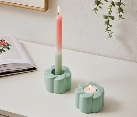 Deux bougeoirs bleu clair en forme de fleur sont posés sur une table, l'un avec une bougie bicolore allumée.