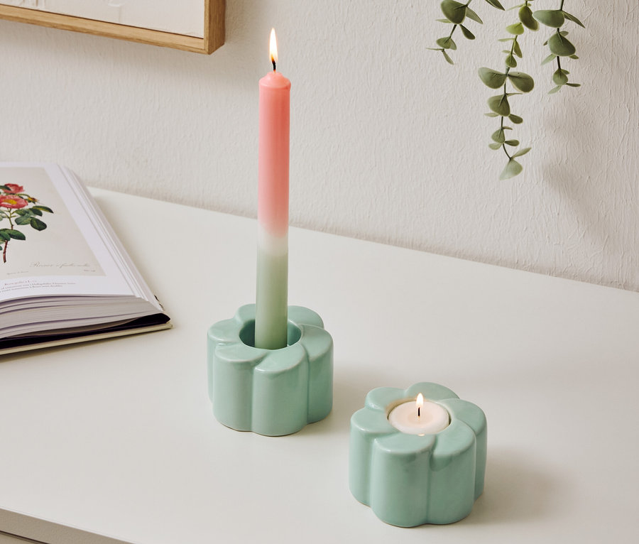 Deux bougeoirs bleu clair en forme de fleur sont posés sur une table, l'un avec une bougie bicolore allumée.