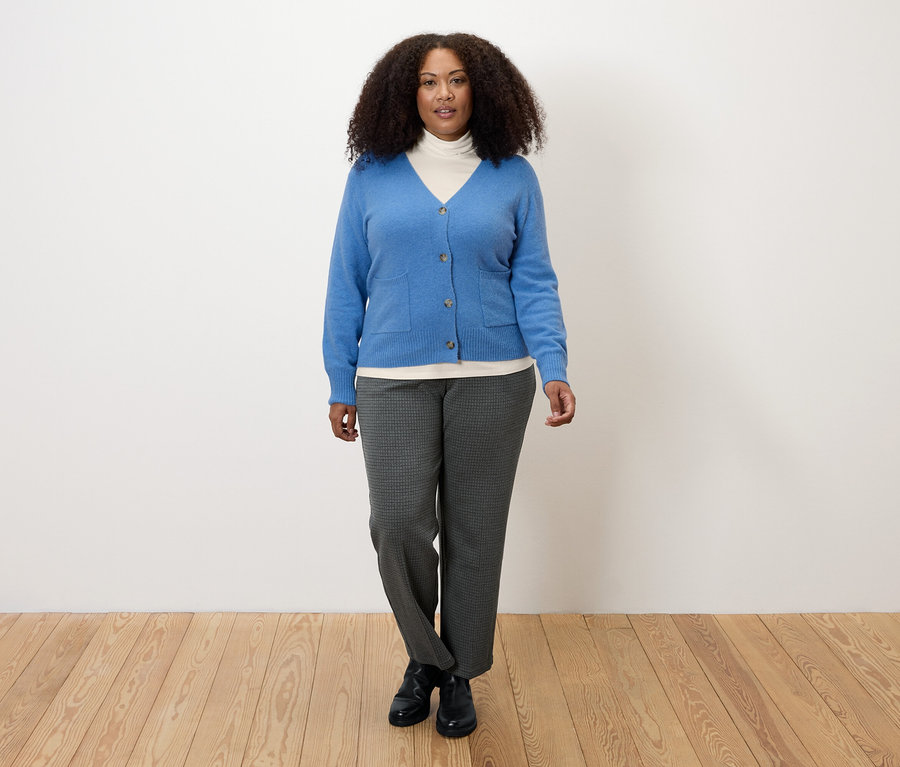 Femme portant un T-shirt col roulé à manches longues blanc crème, un cardigan bleu et un pantalon gris.