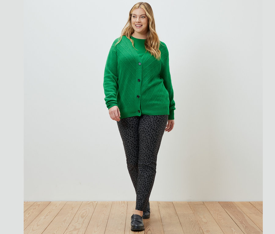 Une femme marche et porte un cardigan vert avec structure tricotée, un haut à manches longues vert et un pantalon imprimé en bengaline.