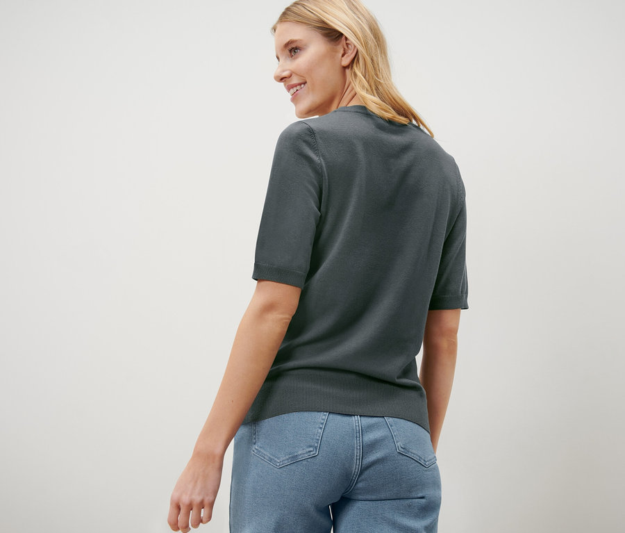 Une femme regardant par-dessus son épaule porte un pull en maille fine vert et un jean.