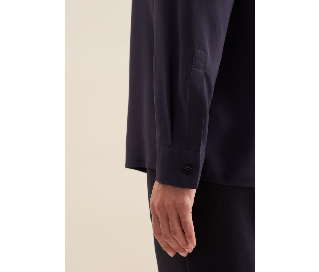 Gros plan sur le bras d'une personne portant une tunique en viscose Seidensticker bleu foncé avec un poignet boutonné, associée à un pantalon foncé.