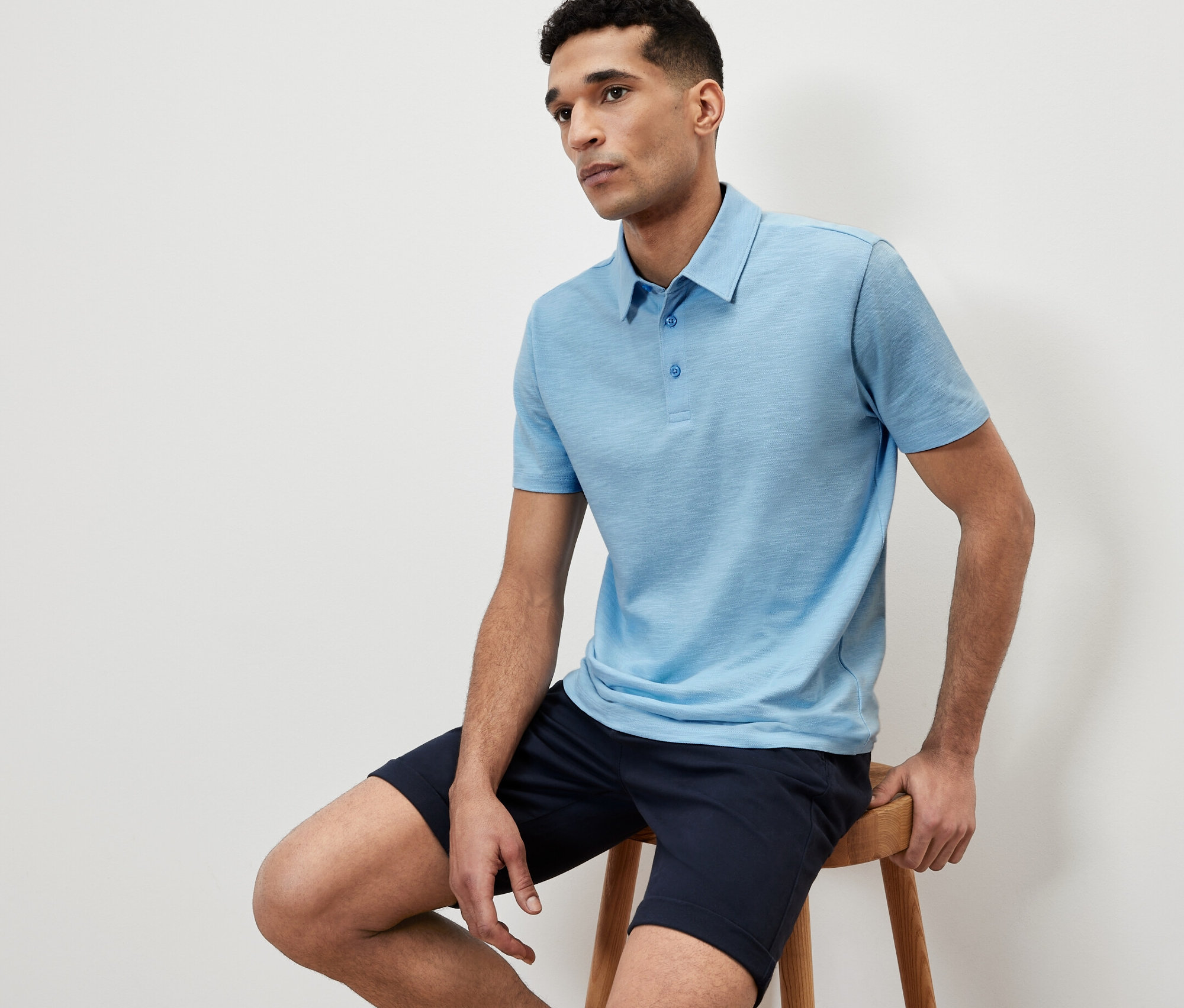 Un homme est assis sur un tabouret et porte un polo bleu.