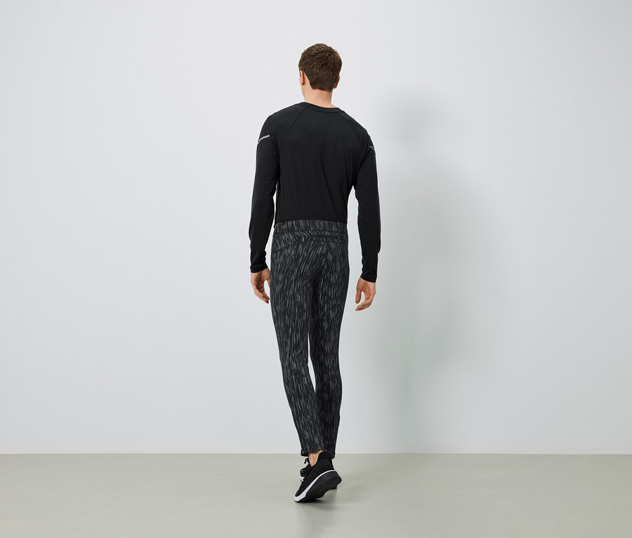 Un homme portant un t-shirt noir à manches longues et un pantalon à motifs, vu de dos.