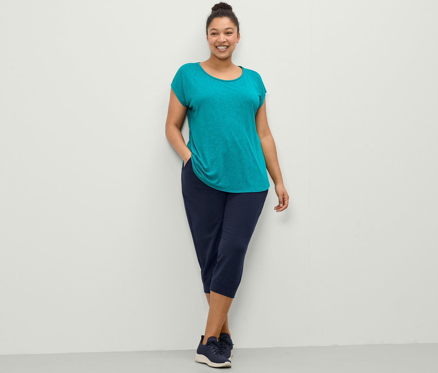 Femme posant en t-shirt de sport turquoise et pantalon sweat 3/4 bleu foncé.