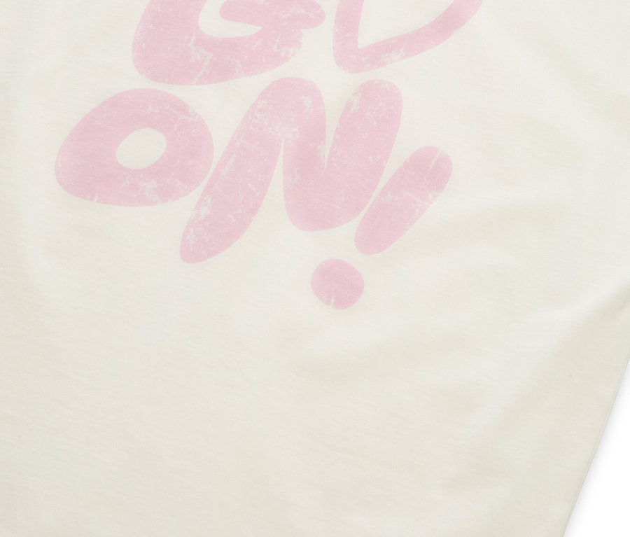 Un t-shirt couleur crème avec l'inscription rose "GO ON !", où le "O" dans "GO" est remplacé par un symbole de cœur.