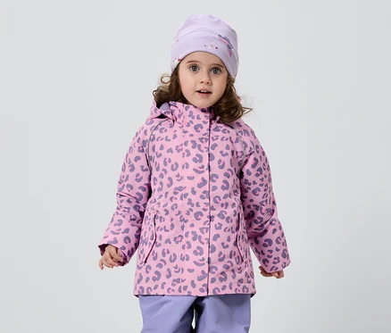 Une petite fille aux cheveux bouclés porte une veste rose et violette à motif léopard, un bonnet assorti et un pantalon violet sur fond blanc.