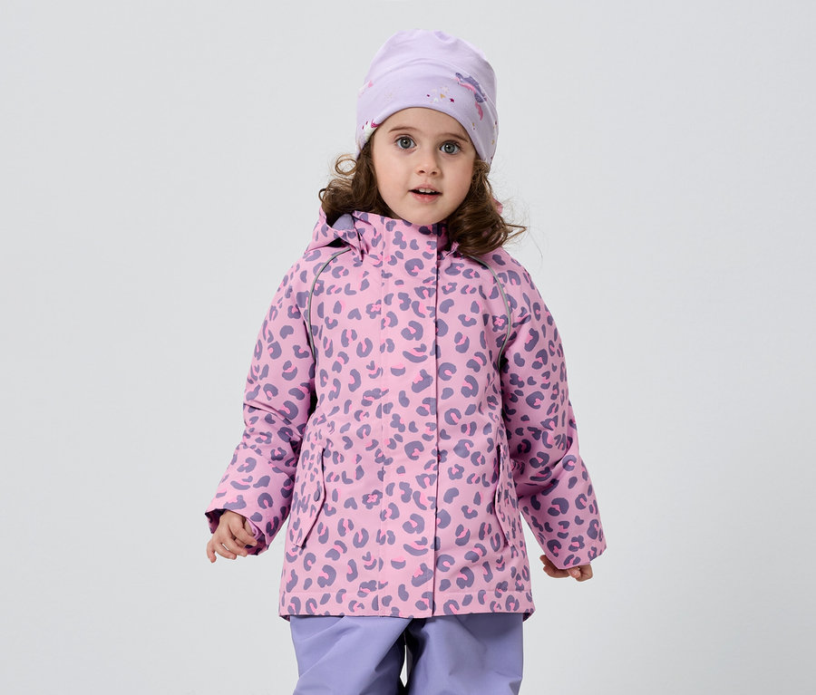 Une petite fille aux cheveux bouclés porte une veste rose et violette à motif léopard, un bonnet assorti et un pantalon violet sur fond blanc.