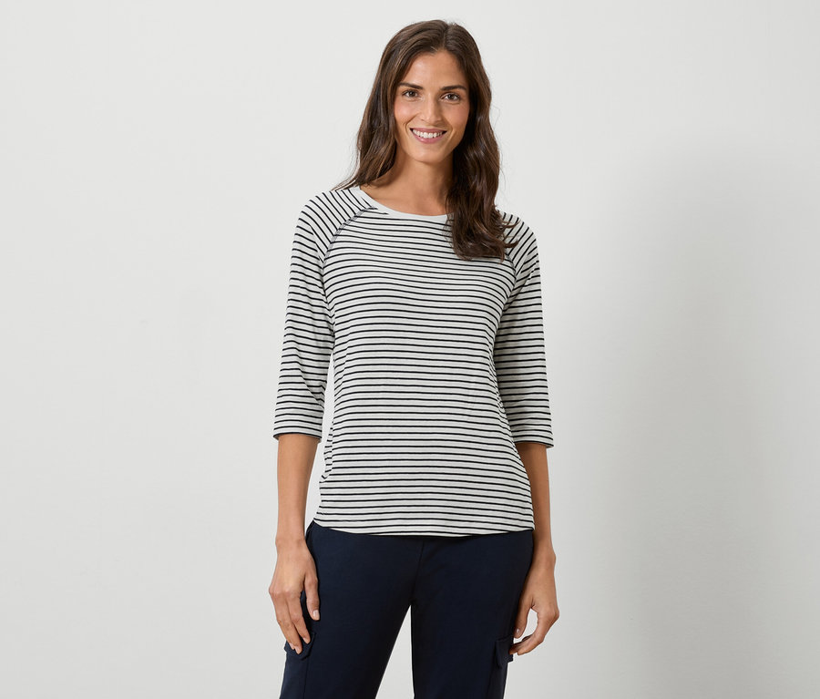 Une femme porte un t-shirt rayé à manches longues et un pantalon bleu marine sur un fond blanc.