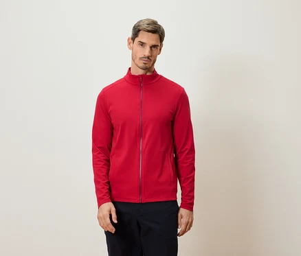 Un homme se tient devant un mur et porte une veste rouge zippée.