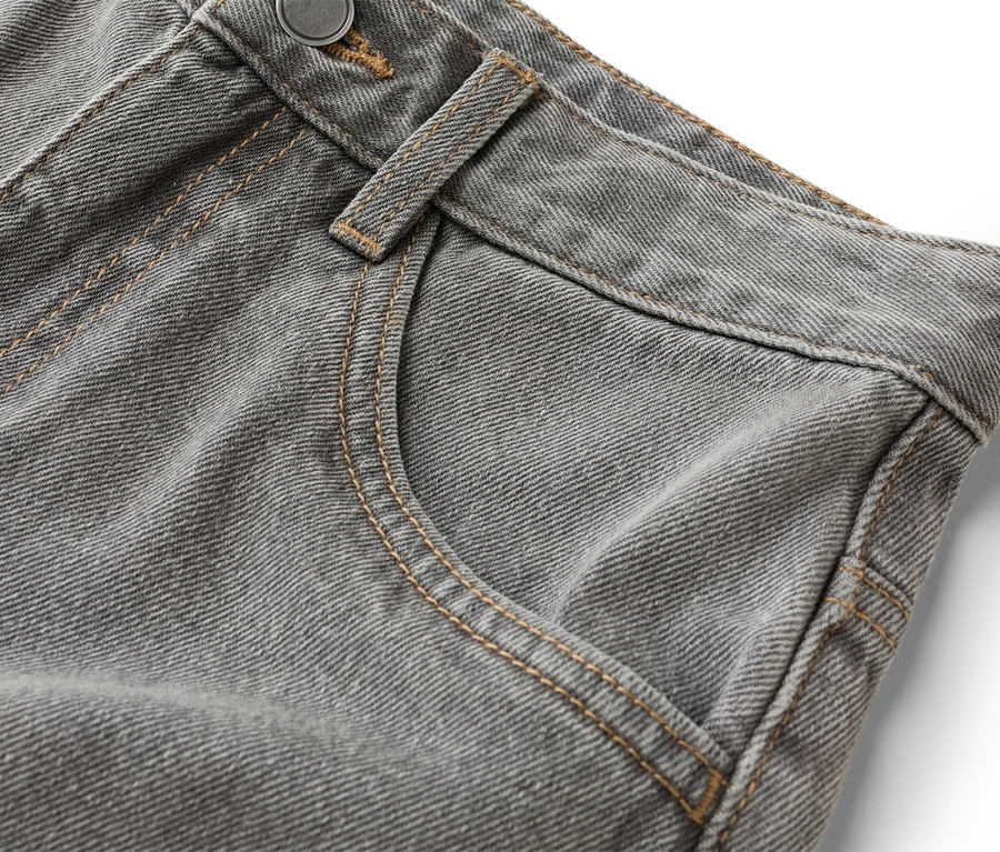 Gros plan sur un jean gris avec poche et bouton.