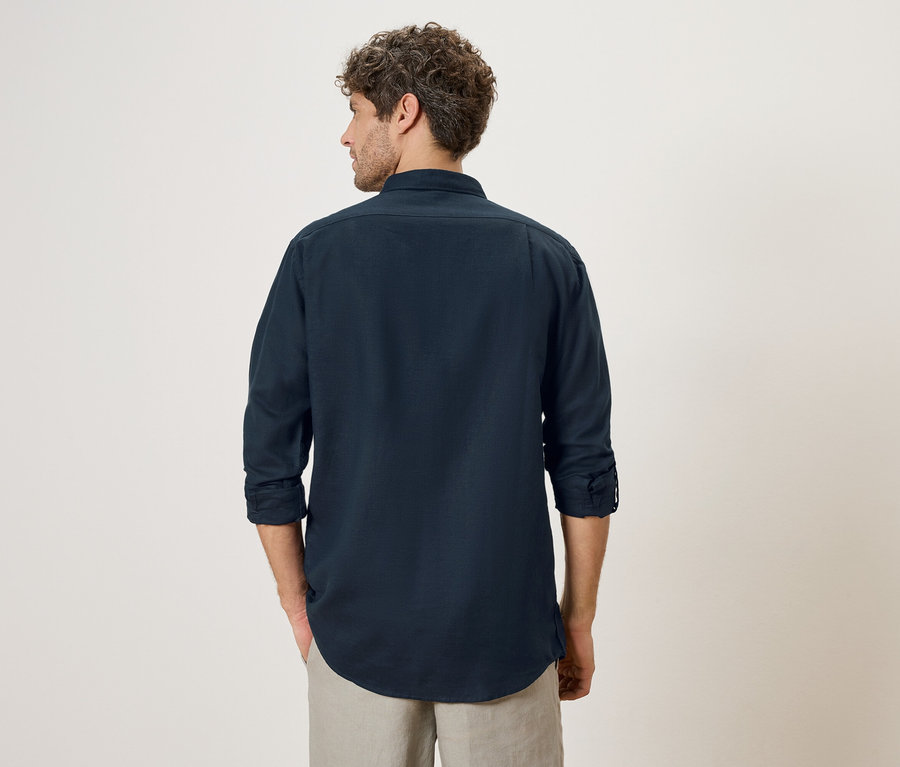 Un homme aux cheveux bouclés, de dos, porte une chemise bleu marine et un short beige.