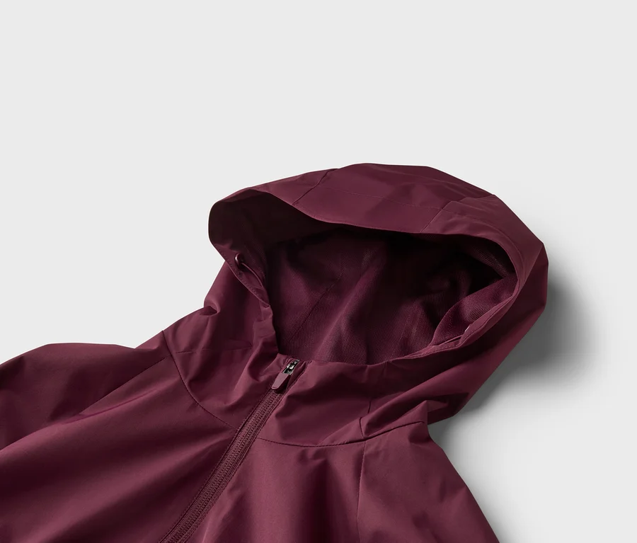 Gros plan d'une veste bordeaux à capuche et fermeture éclair sur fond blanc.