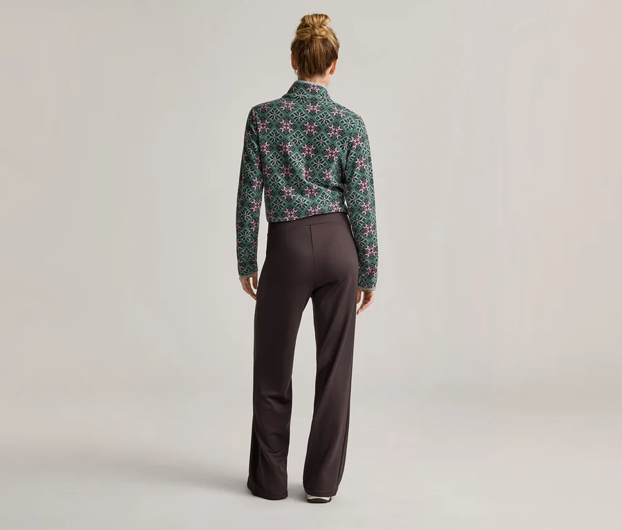 Vue de dos d'une femme avec un chignon portant un haut à manches longues à motifs verts et un pantalon marron.