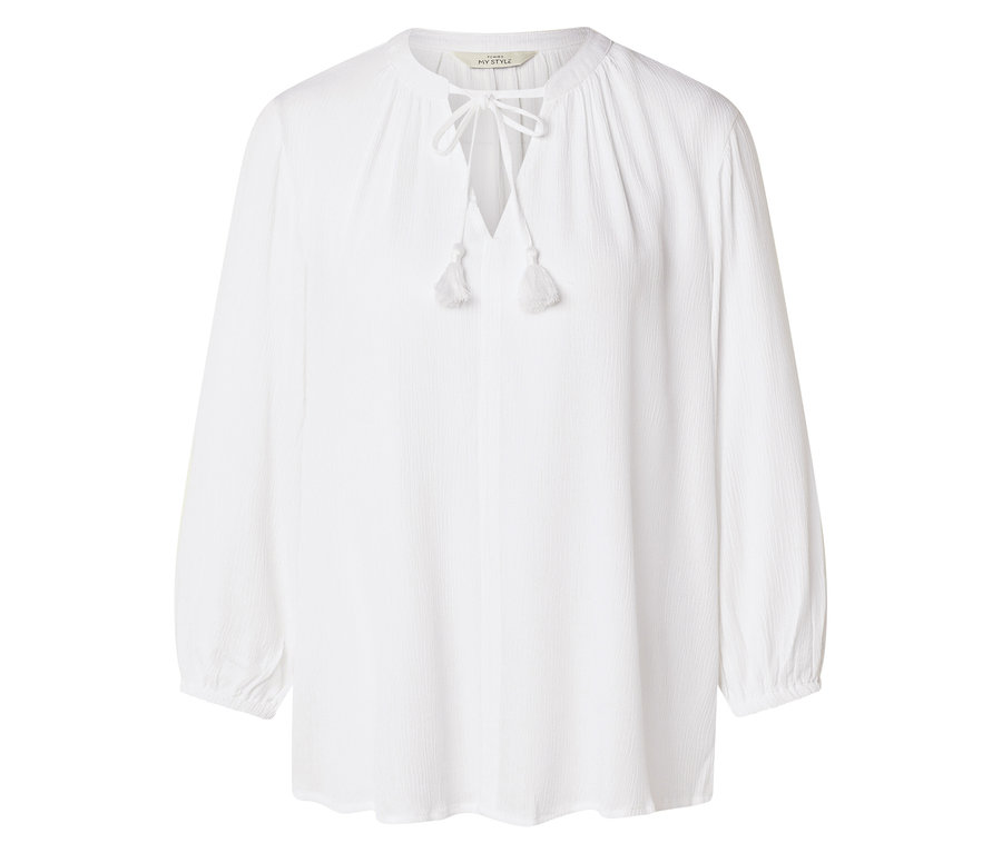 Une chemise blanche à manches longues avec des lacets et des pompons est visible sur un fond blanc.