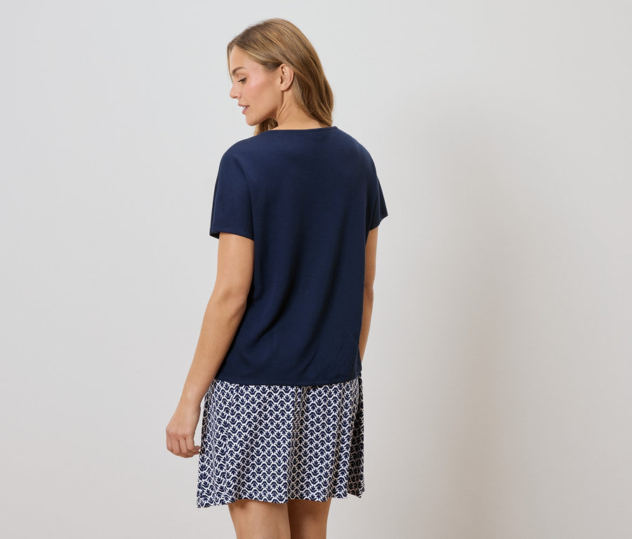 Vue de dos d'une femme blonde portant un t-shirt bleu marine et une jupe à motifs bleu et blanc.