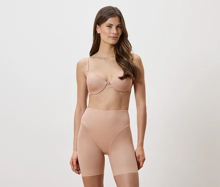 Une femme porte un soutien-gorge couleur chair et un short sculptant sur fond blanc.