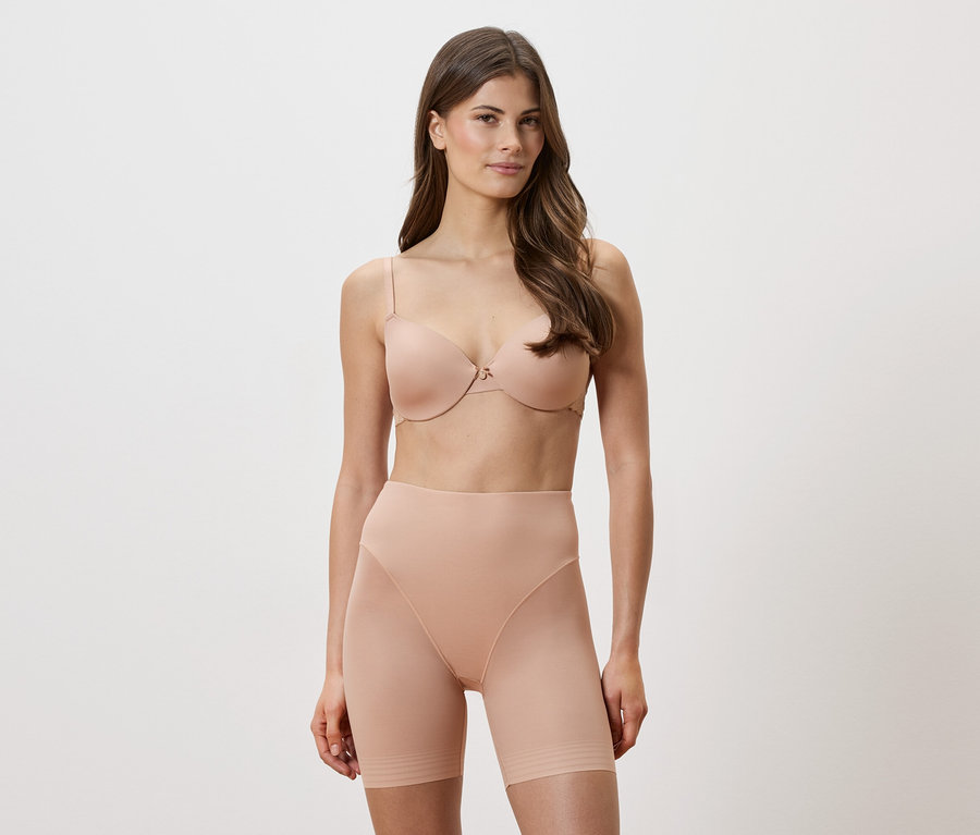 Une femme porte un soutien-gorge couleur chair et un short sculptant sur fond blanc.