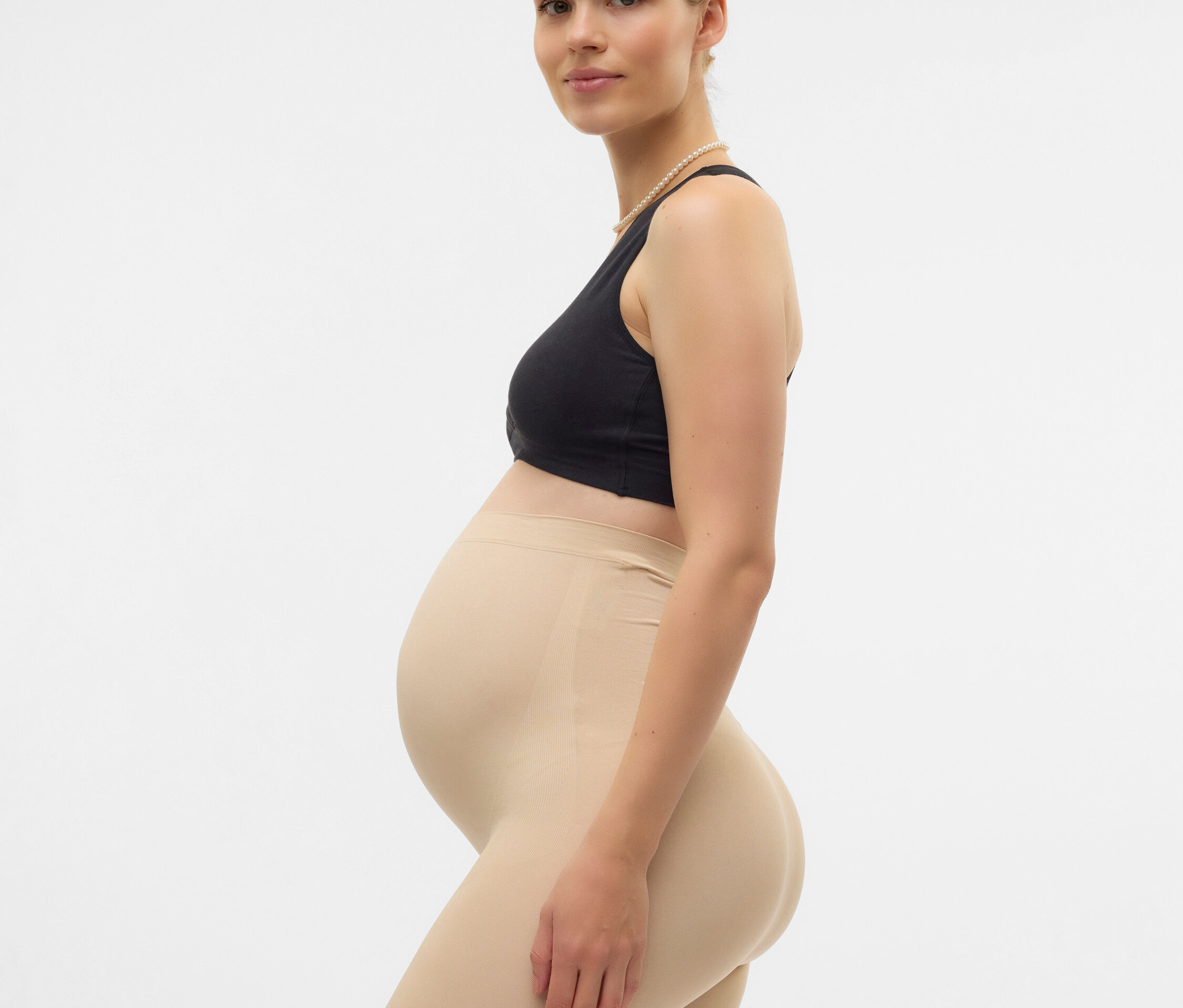 Femme enceinte, debout de profil, portant un soutien-gorge noir et un shorty shapewear couleur chair arrivant au genou.