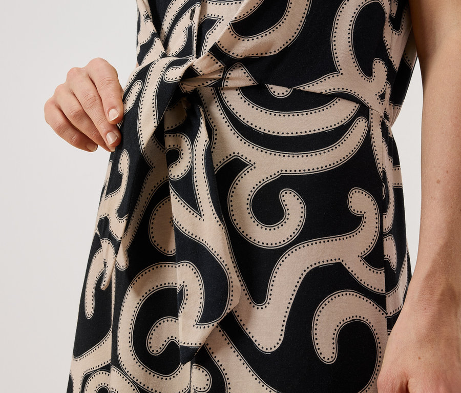 Gros plan d'une femme portant une robe à motifs avec un détail portefeuille et une ceinture nouée.