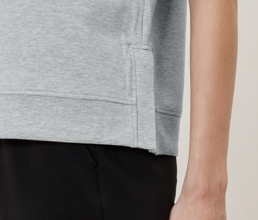 Vue détaillée d'une personne portant un pull gris clair et un pantalon noir.