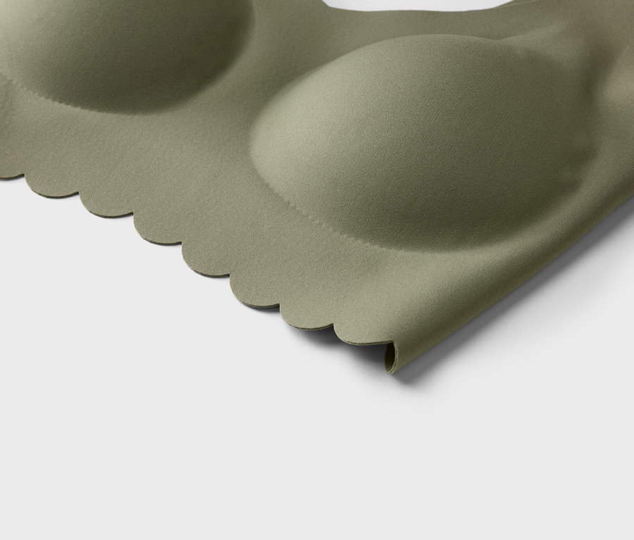 Gros plan d'un soutien-gorge vert olive avec un bord ondulé et des bonnets moulés sur un fond blanc.