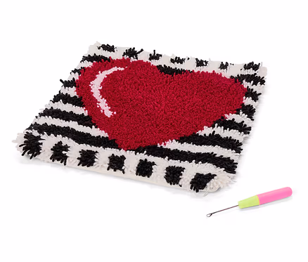 Tapis carré avec un cœur rouge sur un fond rayé noir et blanc et un crochet avec un manche rose et vert.