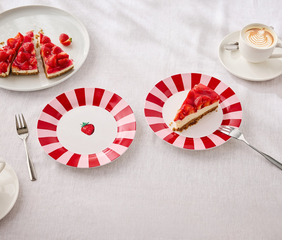 Sur une table, des assiettes avec des gâteaux aux fraises, des fourchettes et des tasses avec du latte art.