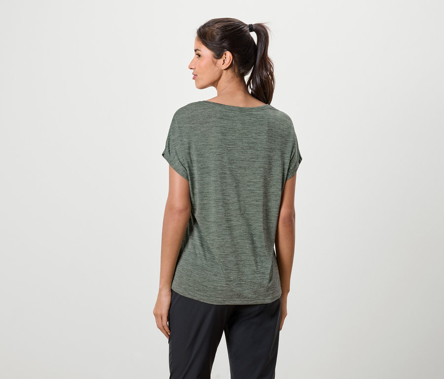 Une femme avec une queue de cheval porte un t-shirt vert et un pantalon noir.