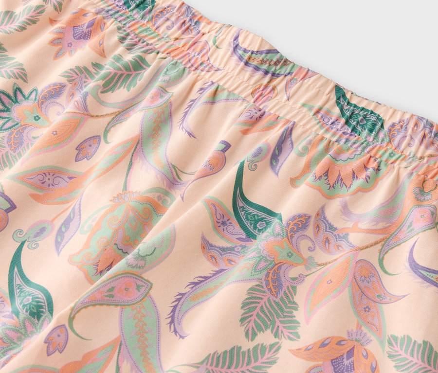 Gros plan d'un tissu pêche clair avec un motif de fleurs et de feuilles dans les tons de vert, de violet et de pêche.